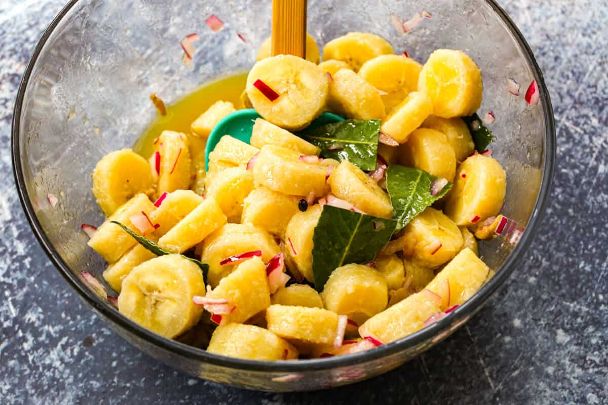 Cooked green bananas in a glass bowl tossed in with a zesty escabeche sauce.