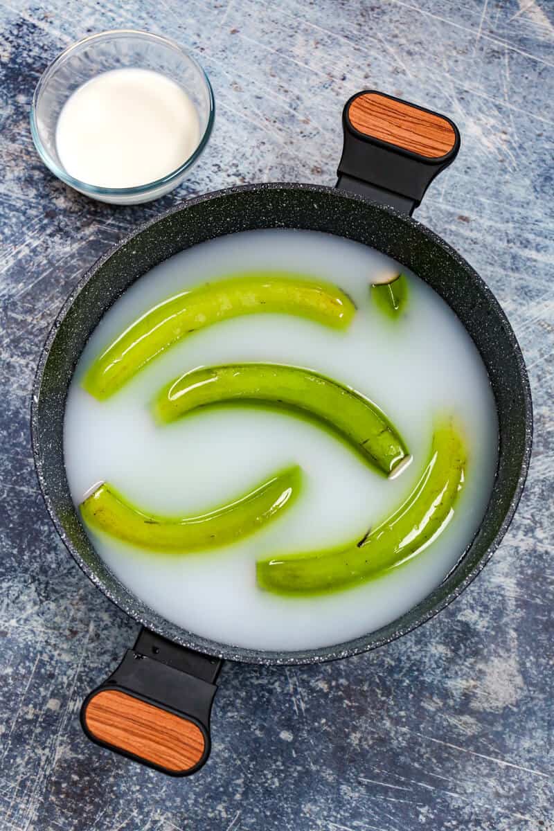 Green bananas in a black pot of water with milk.