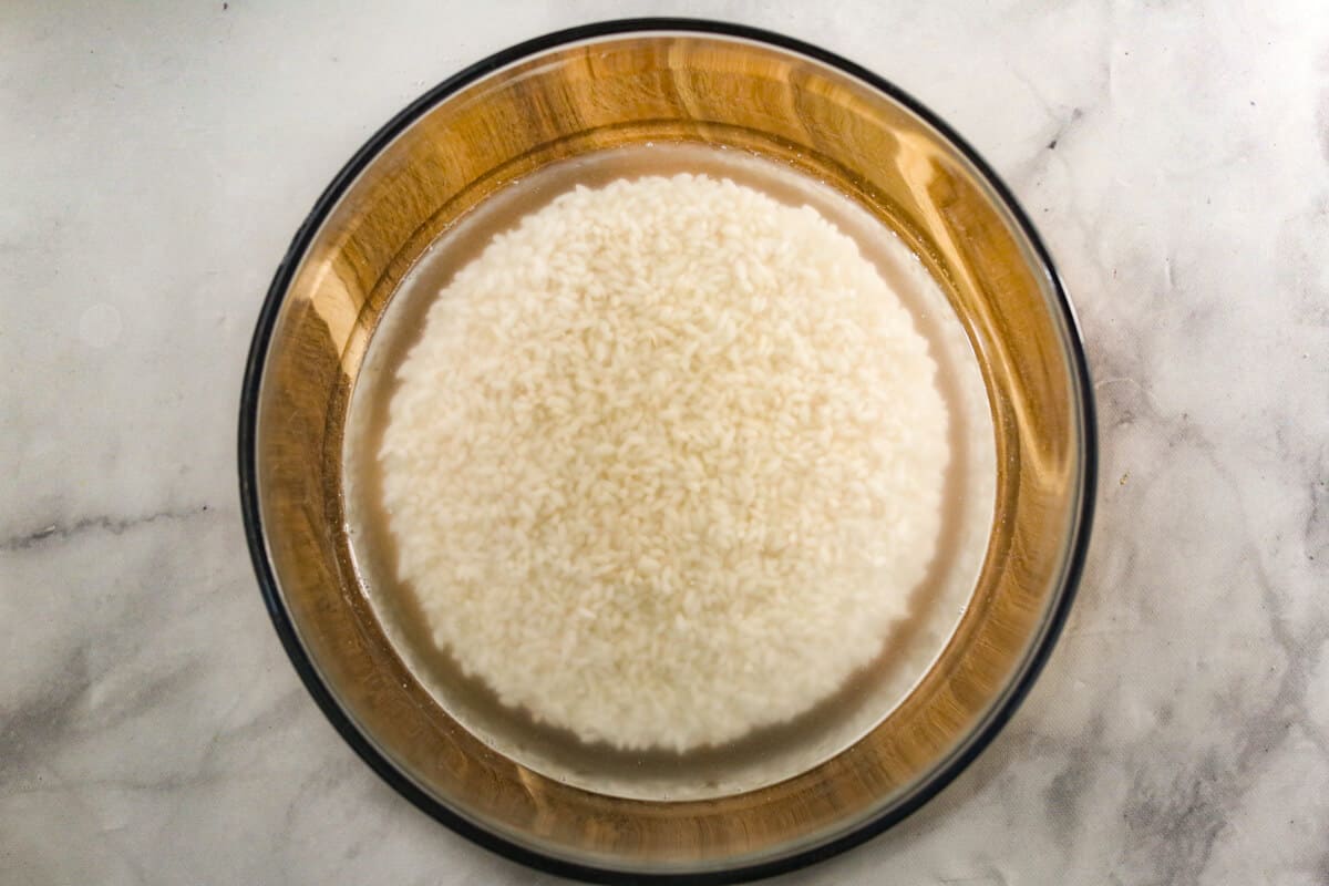 A glass bowl is filled with white rice and water that is soaking.