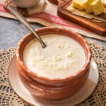A bowl filled with warm and creamy rice milk soup that's known as arroz con leche is centered over an artisan style small bowl with a spoon sitting inside of the soup.