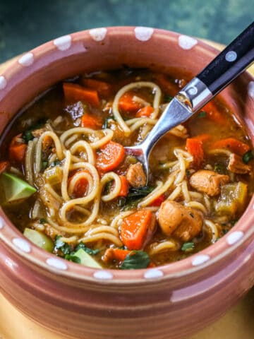 A bowl of noodle soup, known as sopa de fideo is filled with veggies, chicken, and noodles in a rich broth.