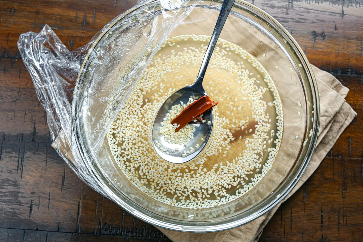 A glass bowl filled with soaked sesame seeds and spices with a metal spoon.