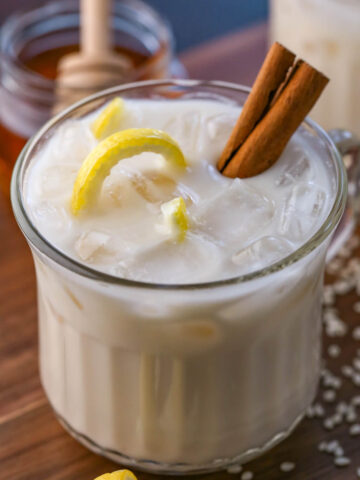 A cup of Puerto Rican horchata is in a glass cup with a cinnamon stick and a sliver of twirling lemon rind for garnish.