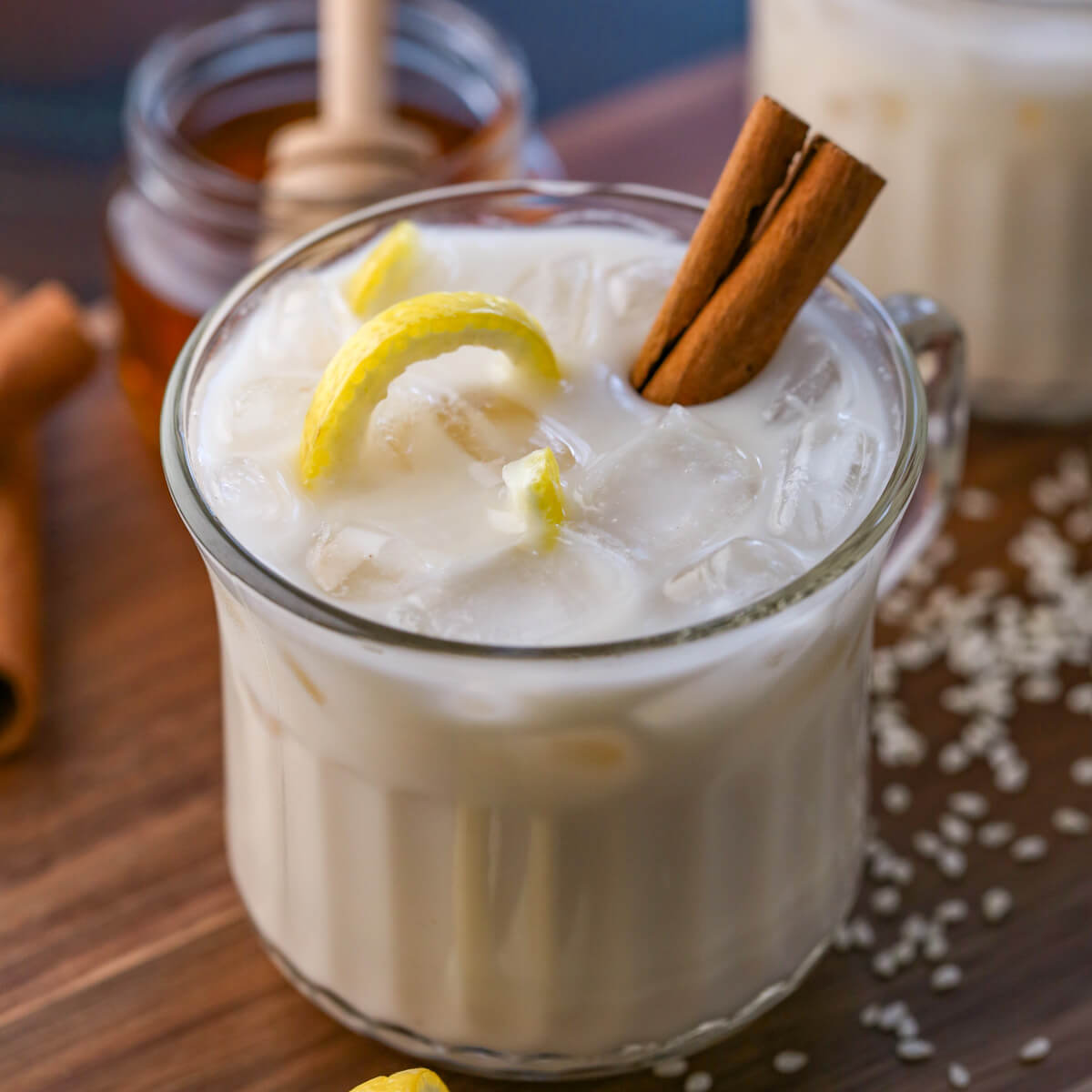 A cup of Puerto Rican horchata is in a glass cup with a cinnamon stick and a sliver of twirling lemon rind for garnish.