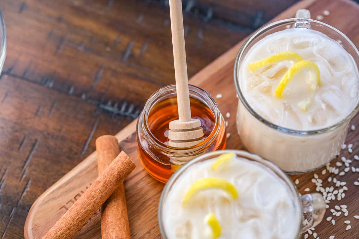 Honey in a small glass pot with a wooden honey stick next to Puerto Rican horchata.