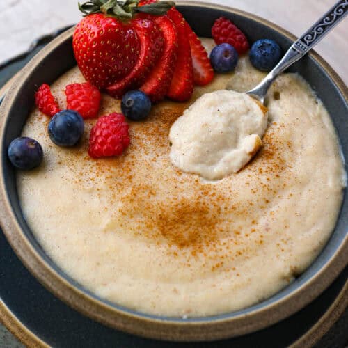 A close up shot of crema de maiz inside of a bowl with a spoon, topped with fresh berries.