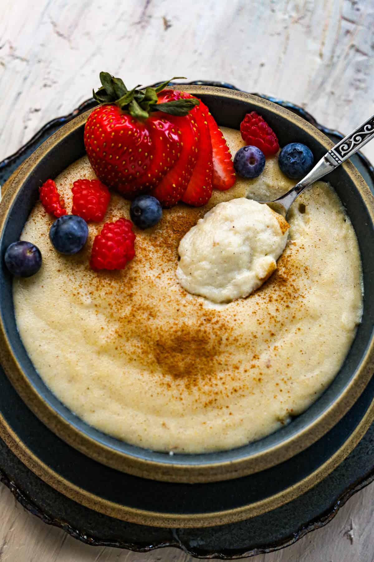 A blue bowl is filled with harina de maiz topped with ground cinnamon and fresh fruit.