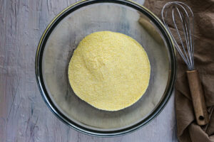 A medium glass bowl has yellow fine cornmeal flour in it.