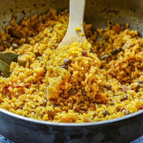 Close up shot of freshly made loose yellow rice and green pigeon peas in a silver pot.