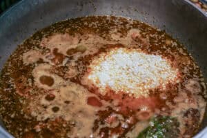 An aluminum caldero is full of sofrito and seasoned broth with white rice to make arroz con gandules.