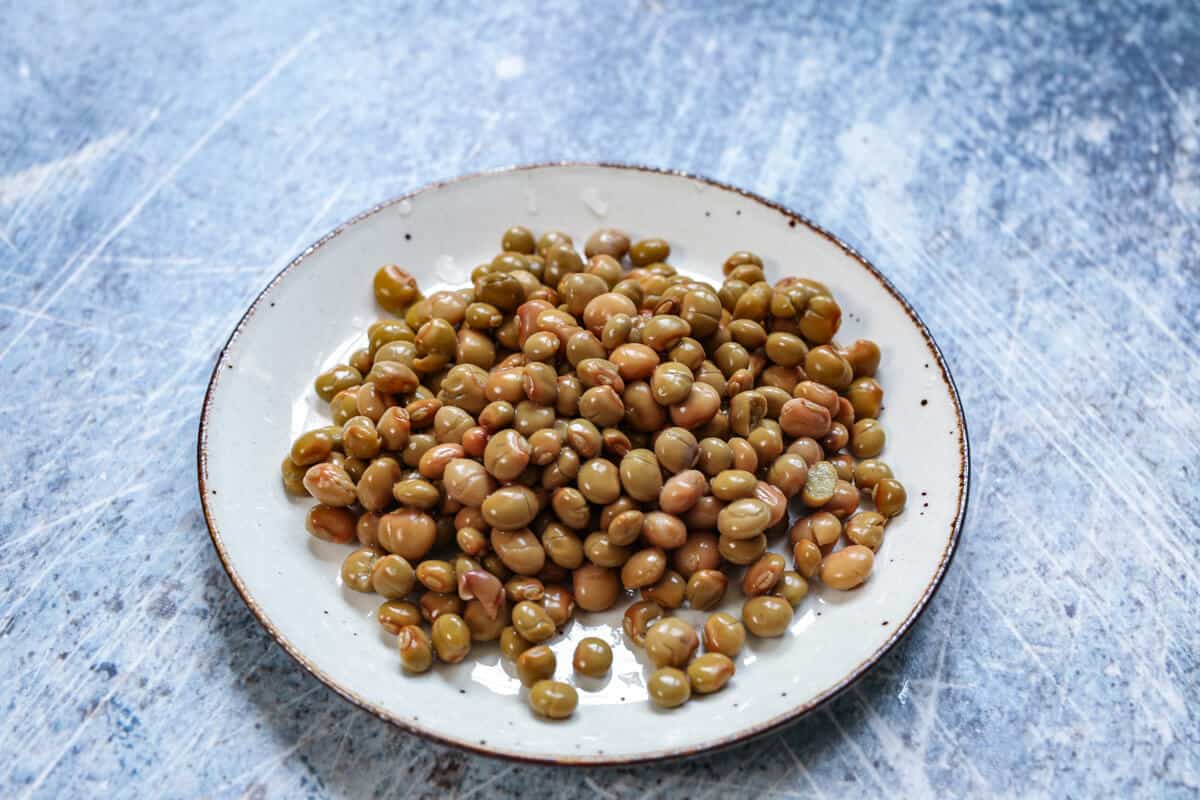 A small white plate is filled with garbanzo beans with a blue background.