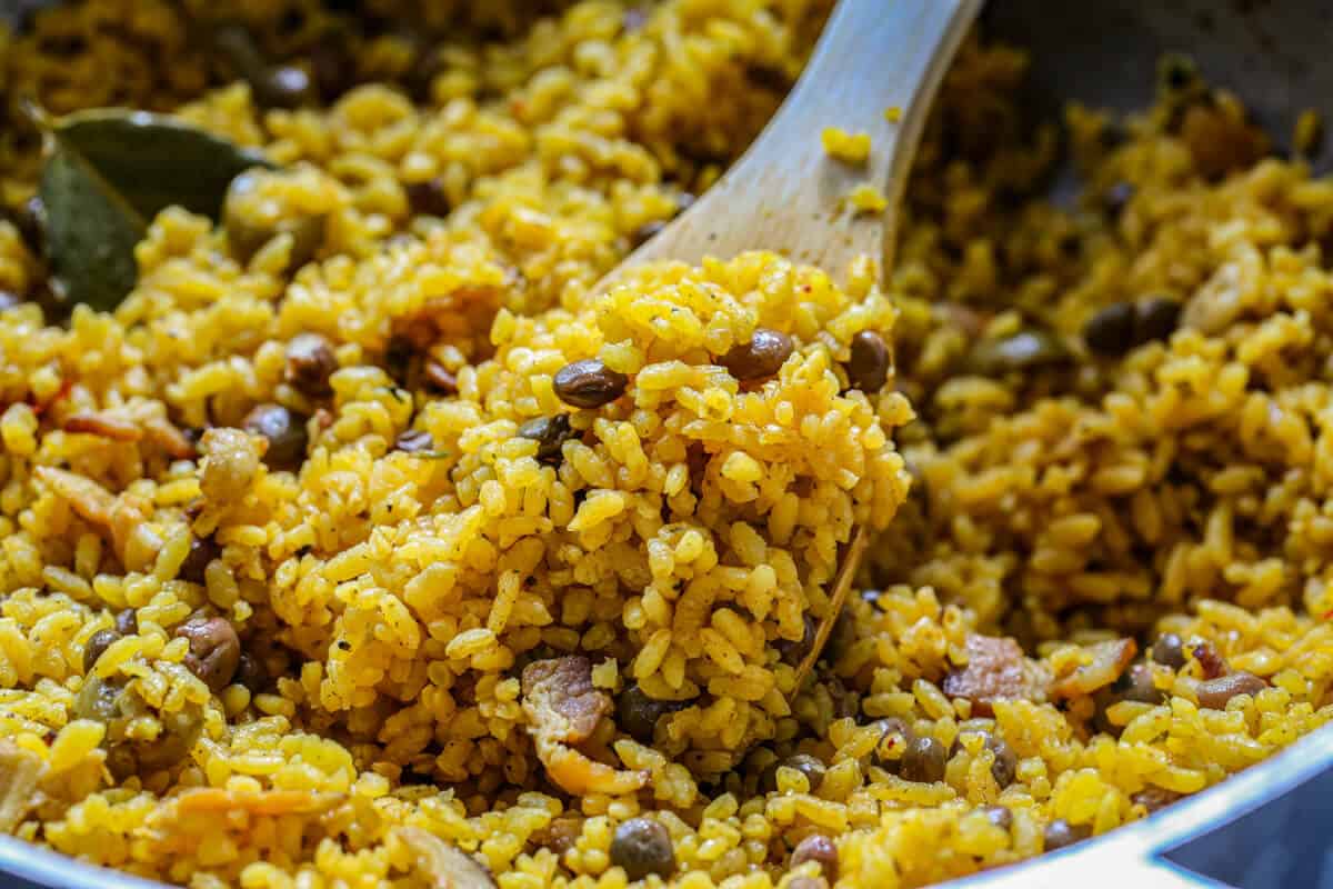 A close up image of arroz con gandules in a caldero with a wooden spoon.