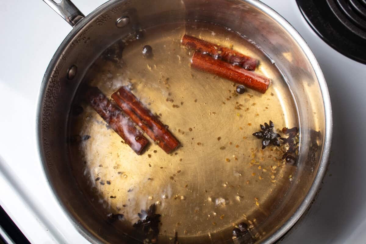 A small pot is filled with boiling water and spices to make tea for coquito.