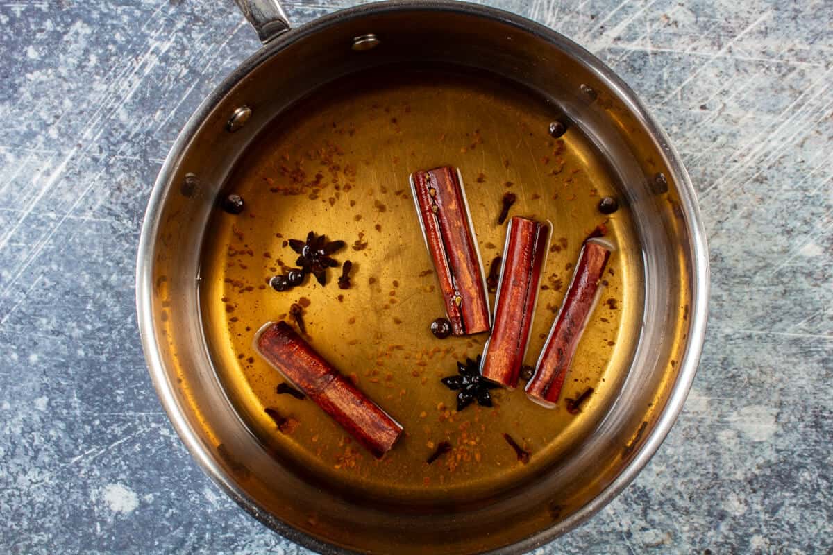 A small metal pan is filled with spices and an amber colored spice tea that's used to make coquito.