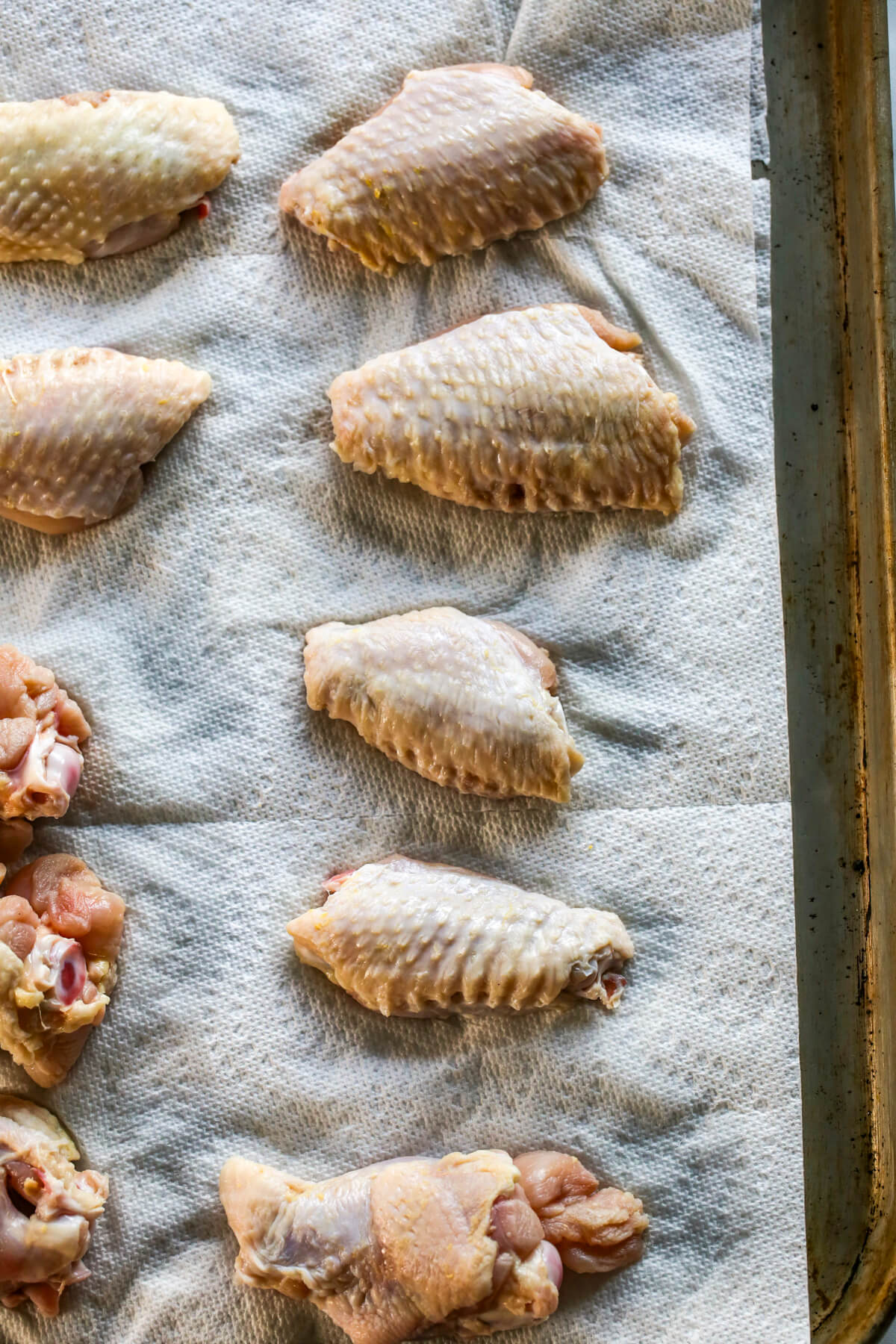 Sheet pan lined with white paper towels with a layer of raw chicken wings on top.