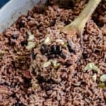 Close up of black rice and black beans in a metal pot with a wooden spoon.