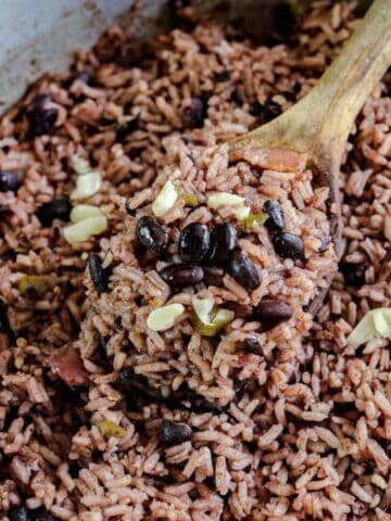 Close up of black rice and black beans in a metal pot with a wooden spoon.
