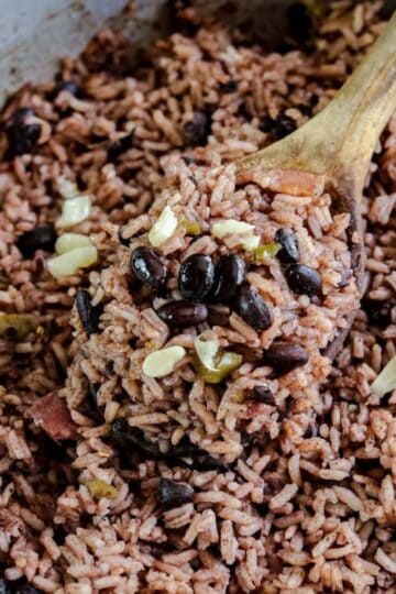 Close up of black rice and black beans in a metal pot with a wooden spoon.