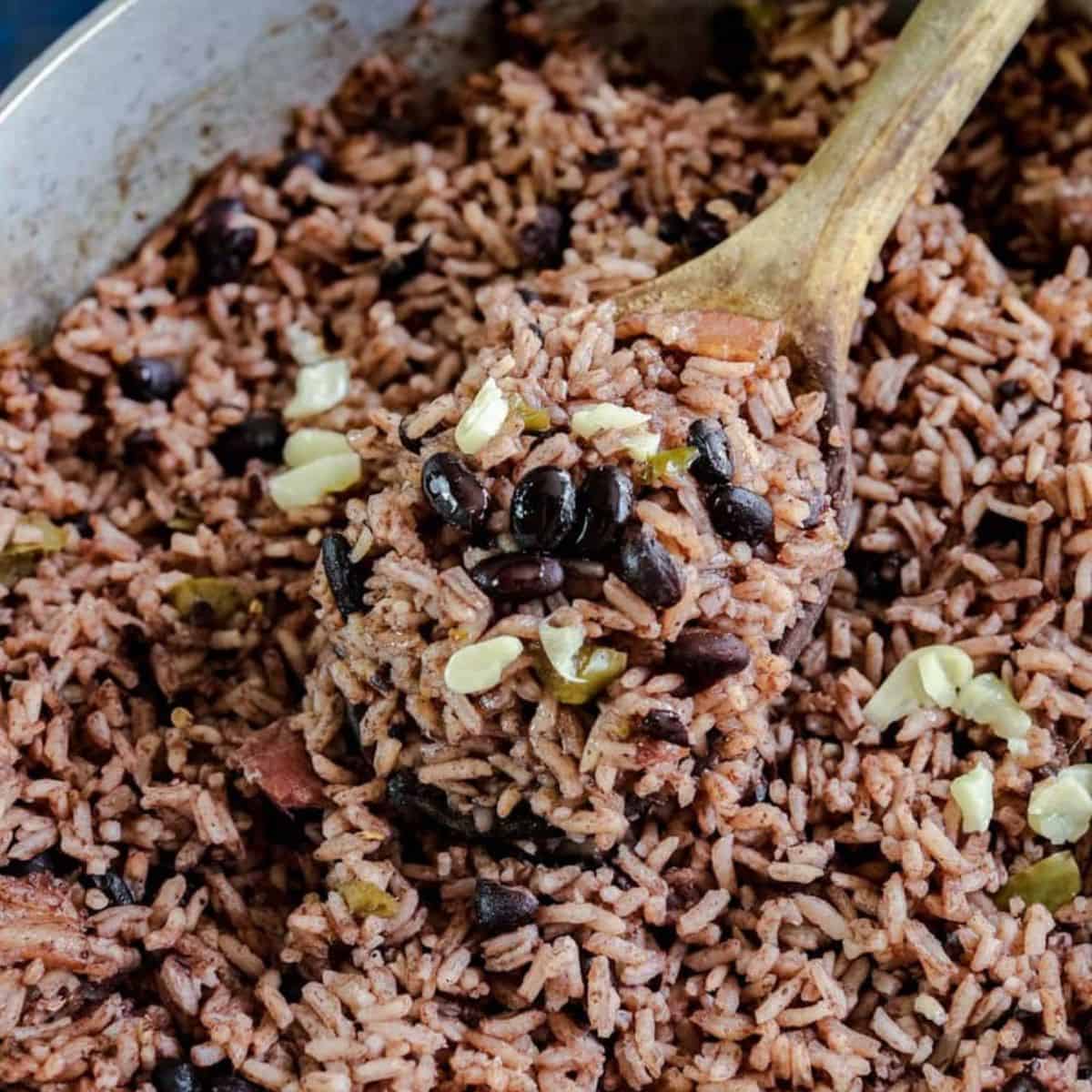 Close up of black rice and black beans in a metal pot with a wooden spoon.