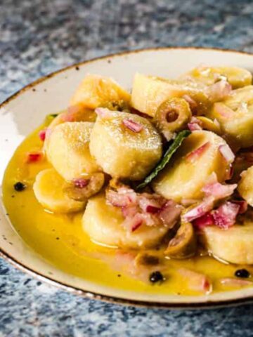 Guineos en escabeche on a white plate with peppercorn, bay leaves, olives, and more!