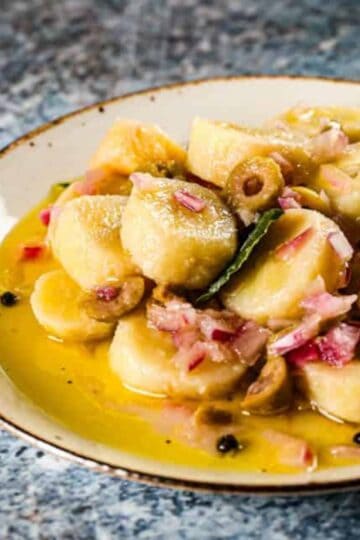 Guineos en escabeche on a white plate with peppercorn, bay leaves, olives, and more!