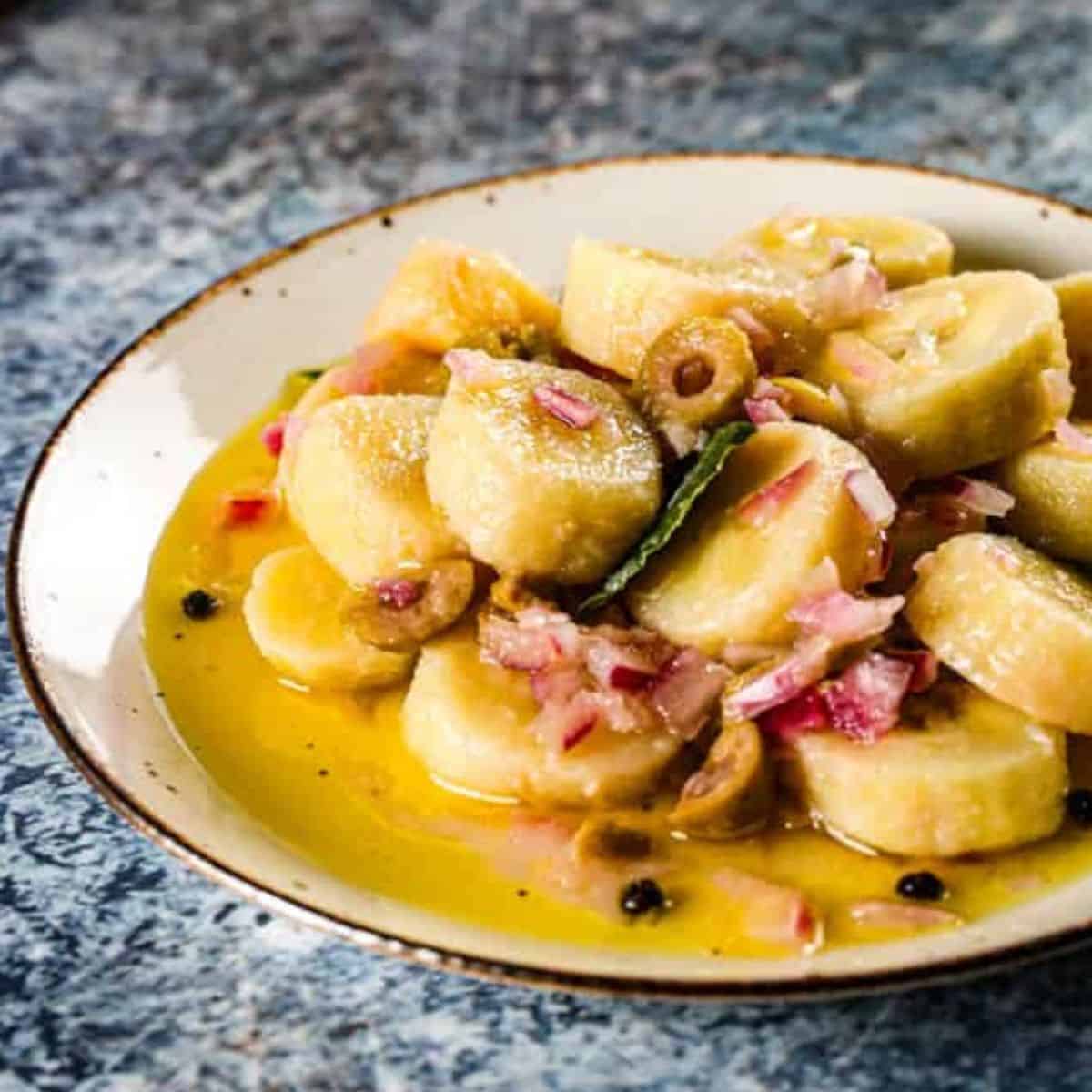 Guineos en escabeche on a white plate with peppercorn, bay leaves, olives, and more!