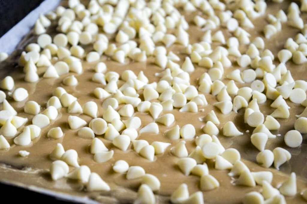 A pan of graham crackers topped with melted toffee, and covered in white chocolate chips, before melting.