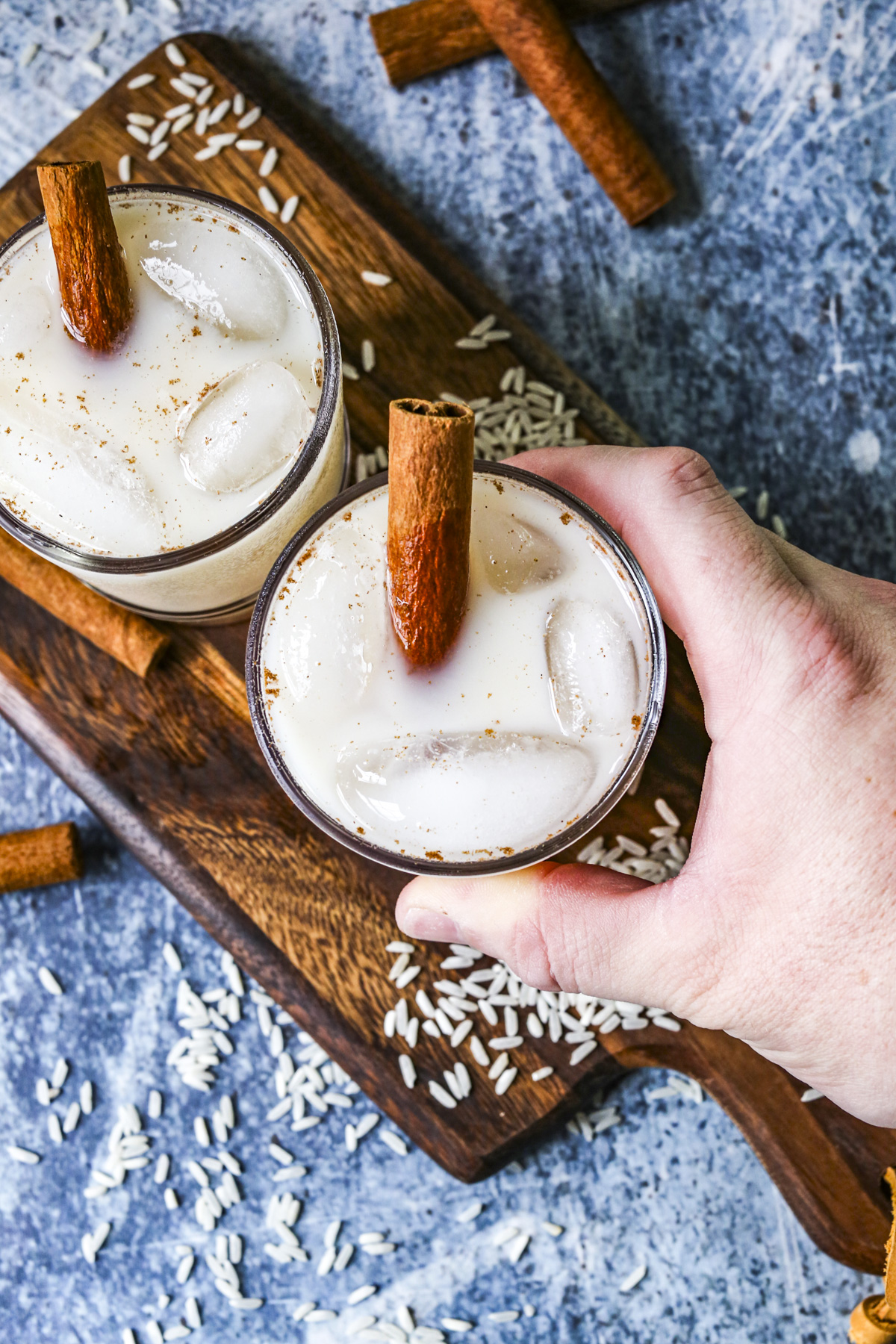 A man's hand is reaching for a glass full of horchata with ice and a cinnamon stick