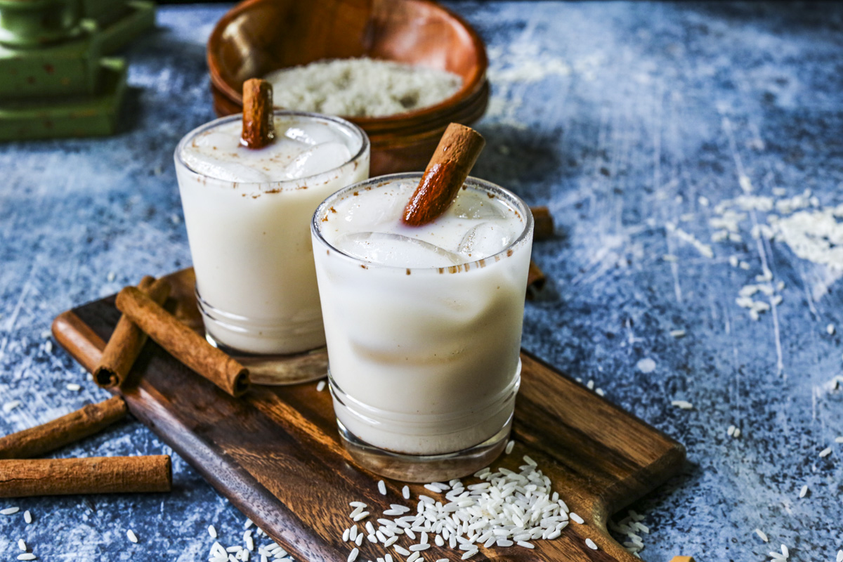 Two cups of horchata are on wooden cutting boards, garnished with cinnamon sticks and rice.