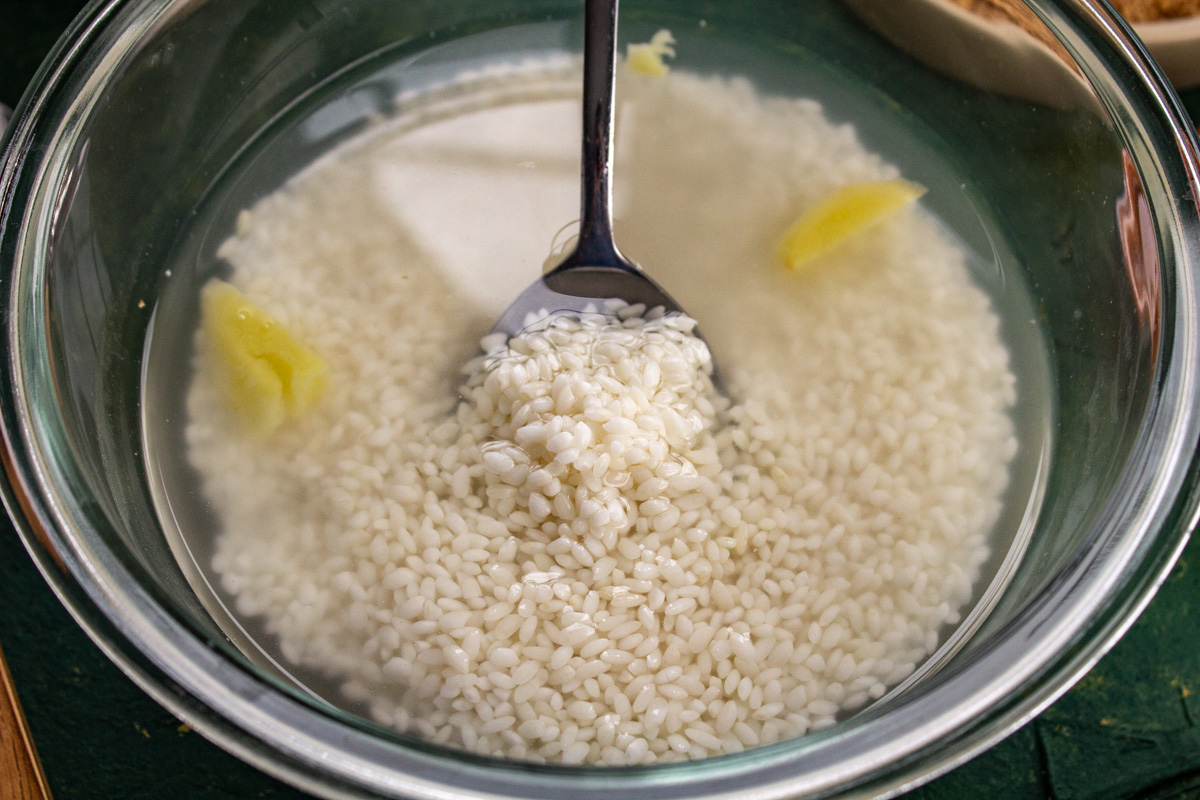 A glass bowl is filled with water, rice, and lemon rinds.