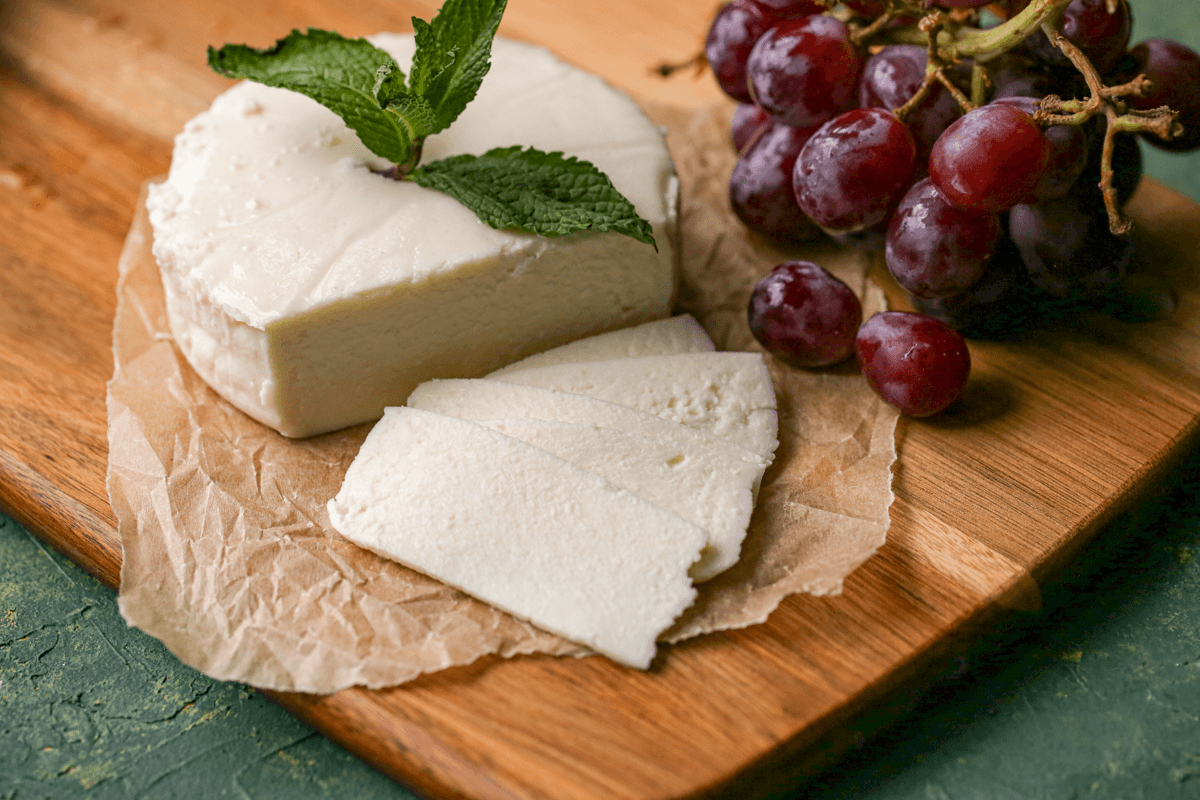 Sliced queso blanco and red grapes are on a wooden cutting board