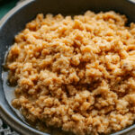 Square close up image of the sweet curds of dulce de leche cortada with the brown syrup in a gray bowl.