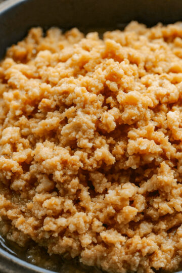 Square close up image of the sweet curds of dulce de leche cortada with the brown syrup in a gray bowl.