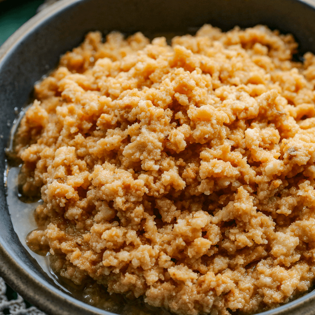 Square close up image of the sweet curds of dulce de leche cortada with the brown syrup in a gray bowl.