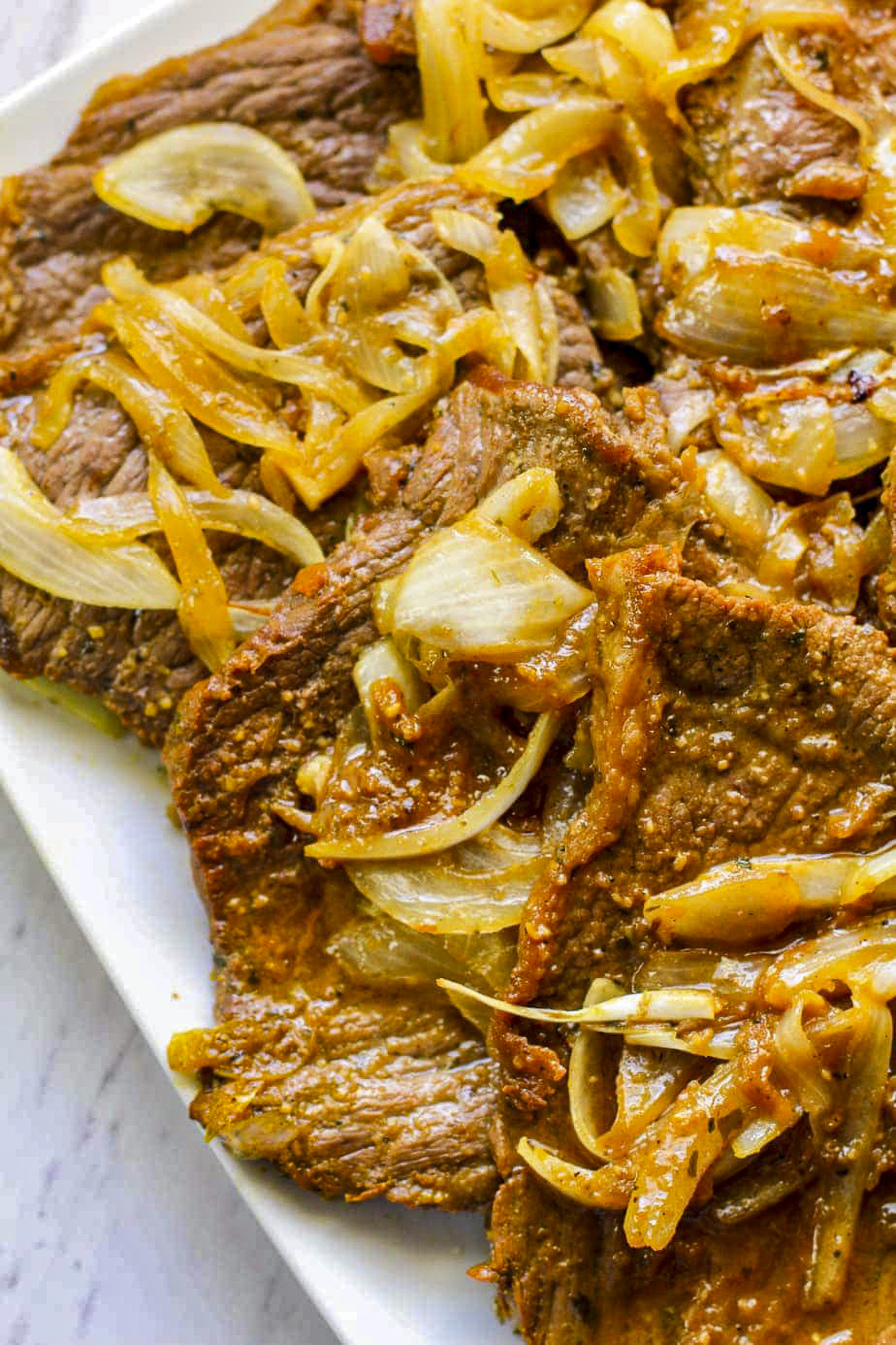 Overhead shot of pan stewed steak and onions on a white plate.
