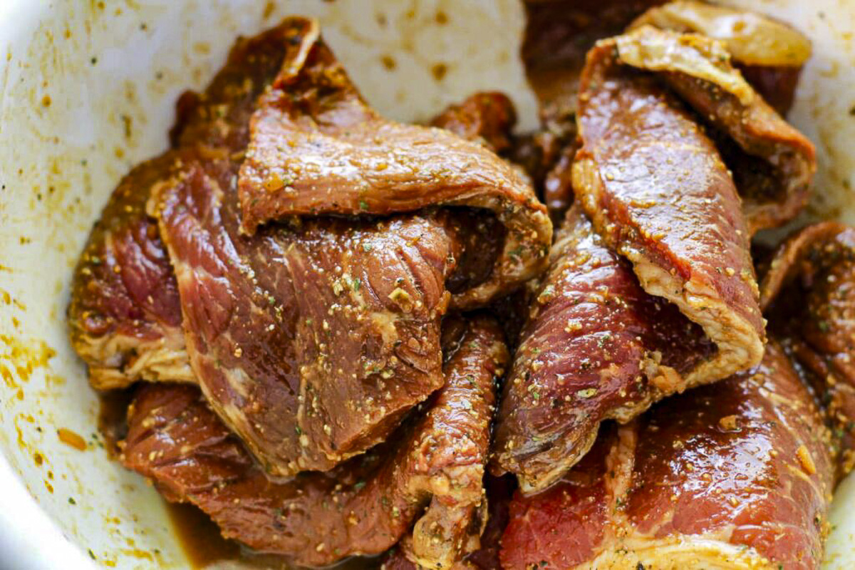 Raw steak marinated in a white bowl.