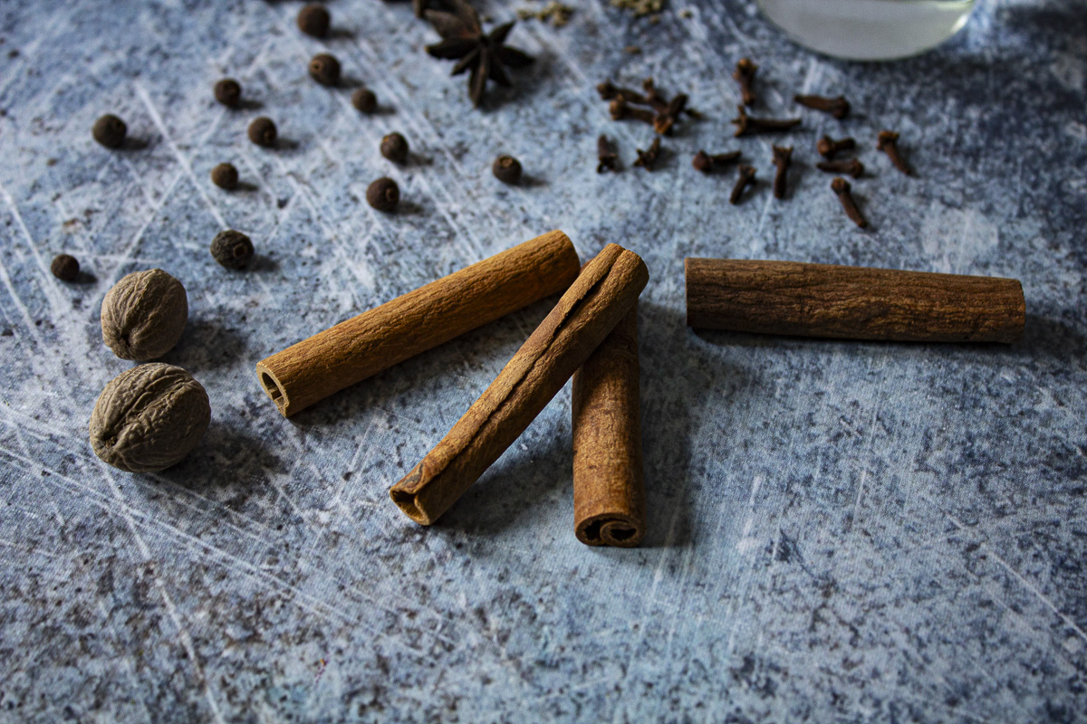 Cinnamon sticks, allspice, cloves, and star anise on a blue background.