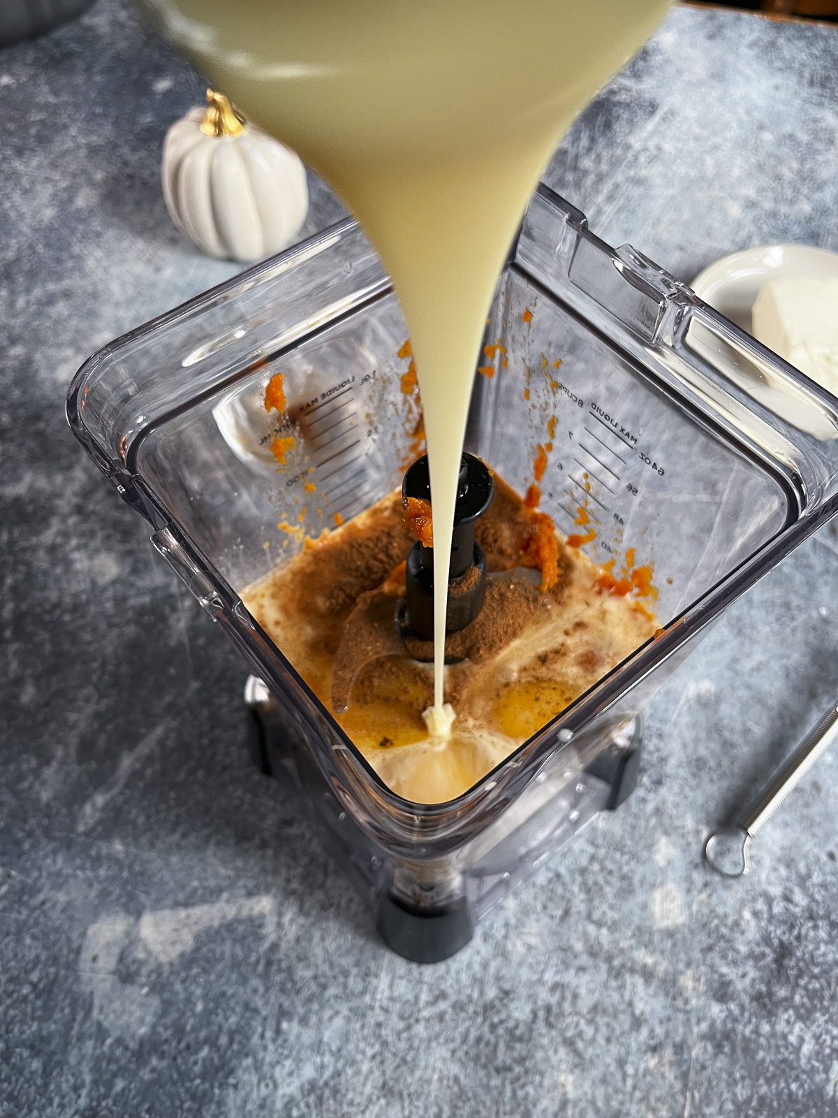 A blender is being filled with ingredients for flan. It's on a blue background.