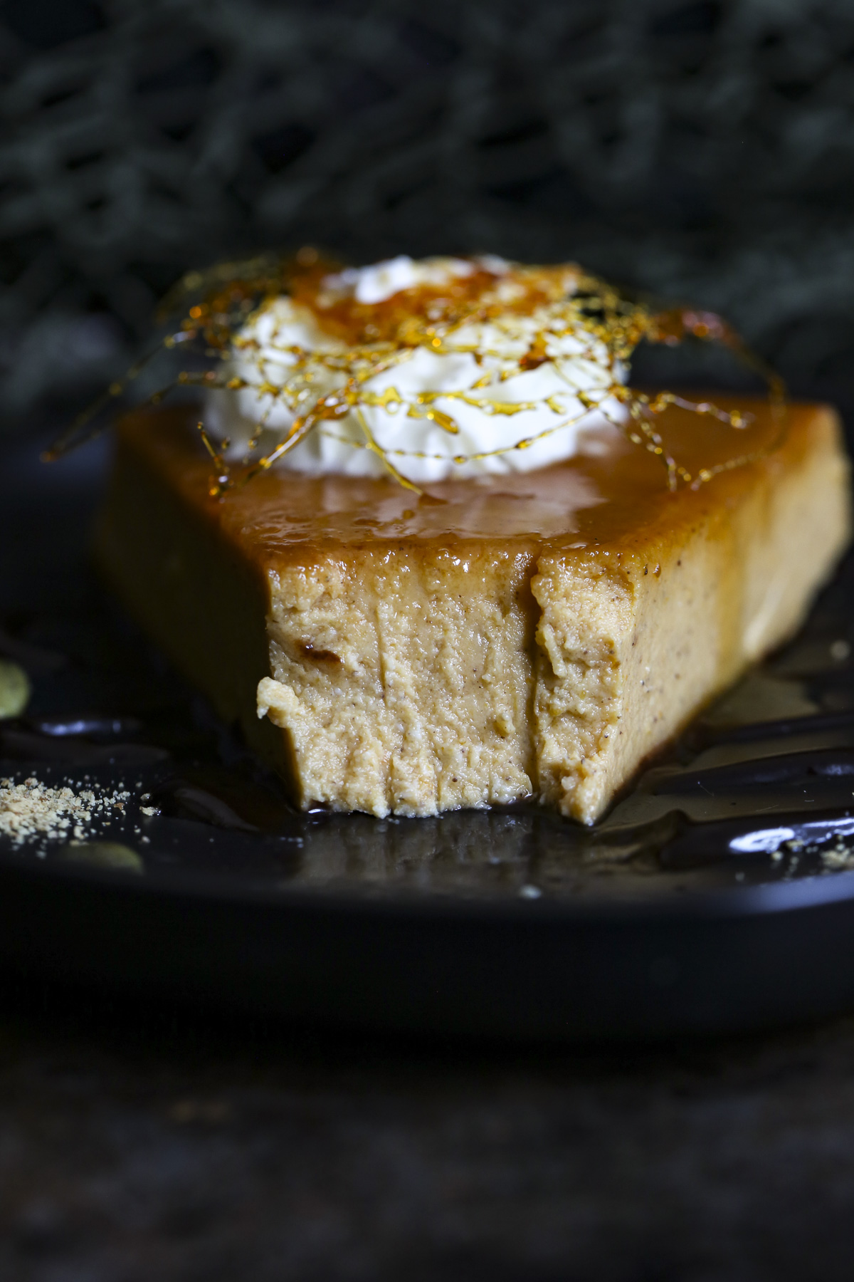 Dark and moody background with a slice of pumpkin flan topped with whip cream and caramel candy