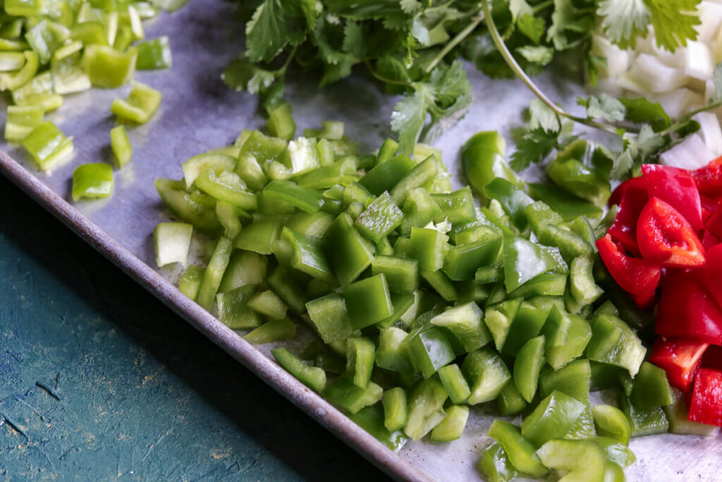 A metal sheet pan is filled with chopped green bell peppers