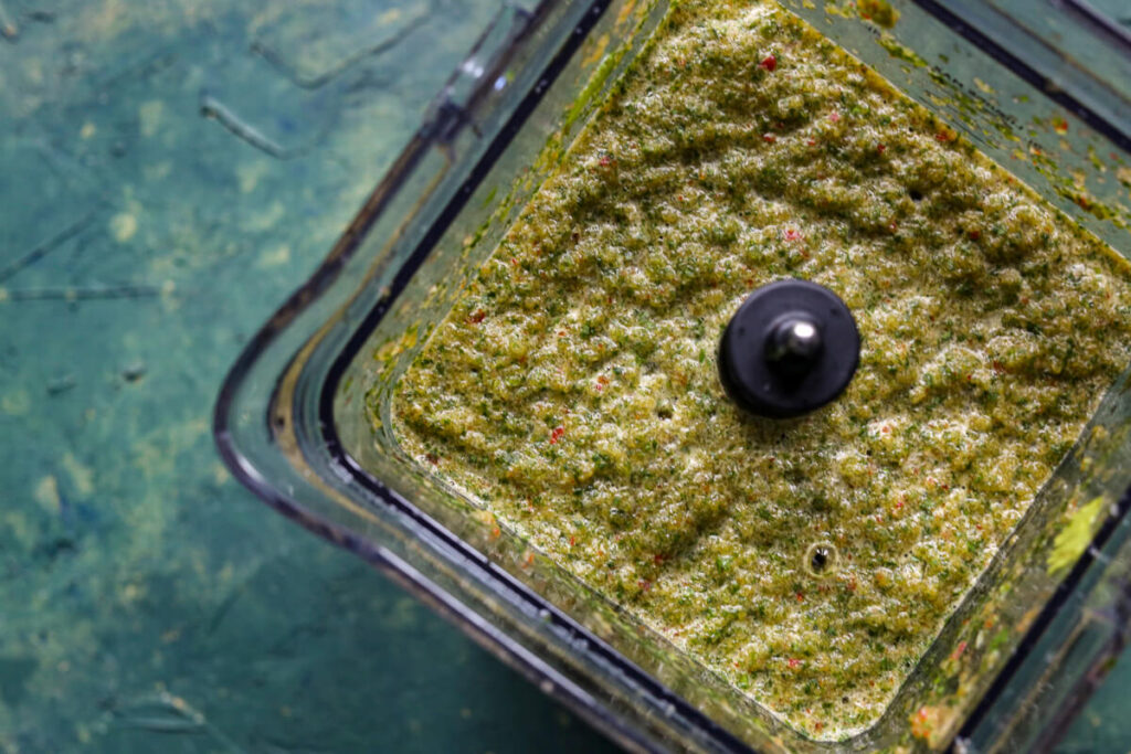 A food processor is filled with pureed sofrito, on a green background.