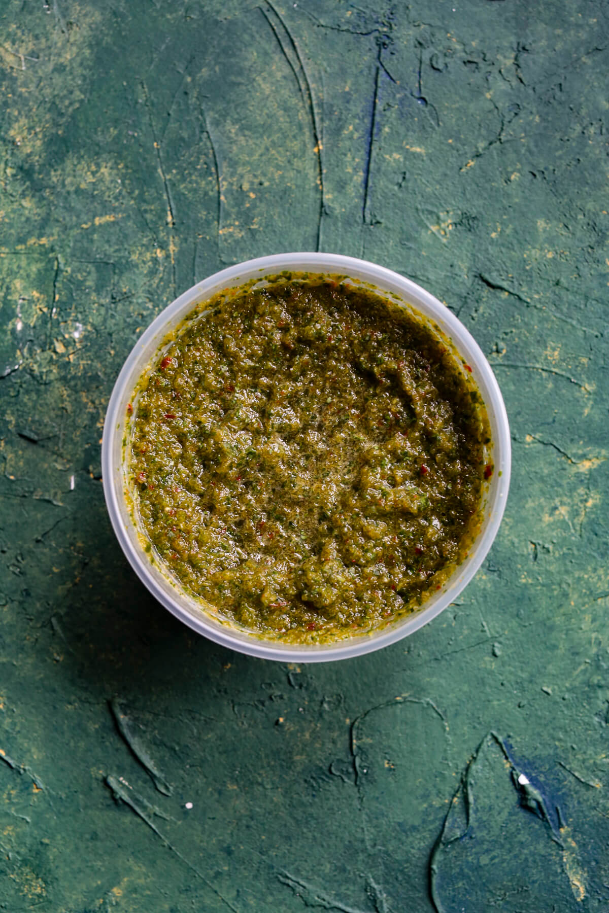 Green background with a plastic clear container filled with green sofrito