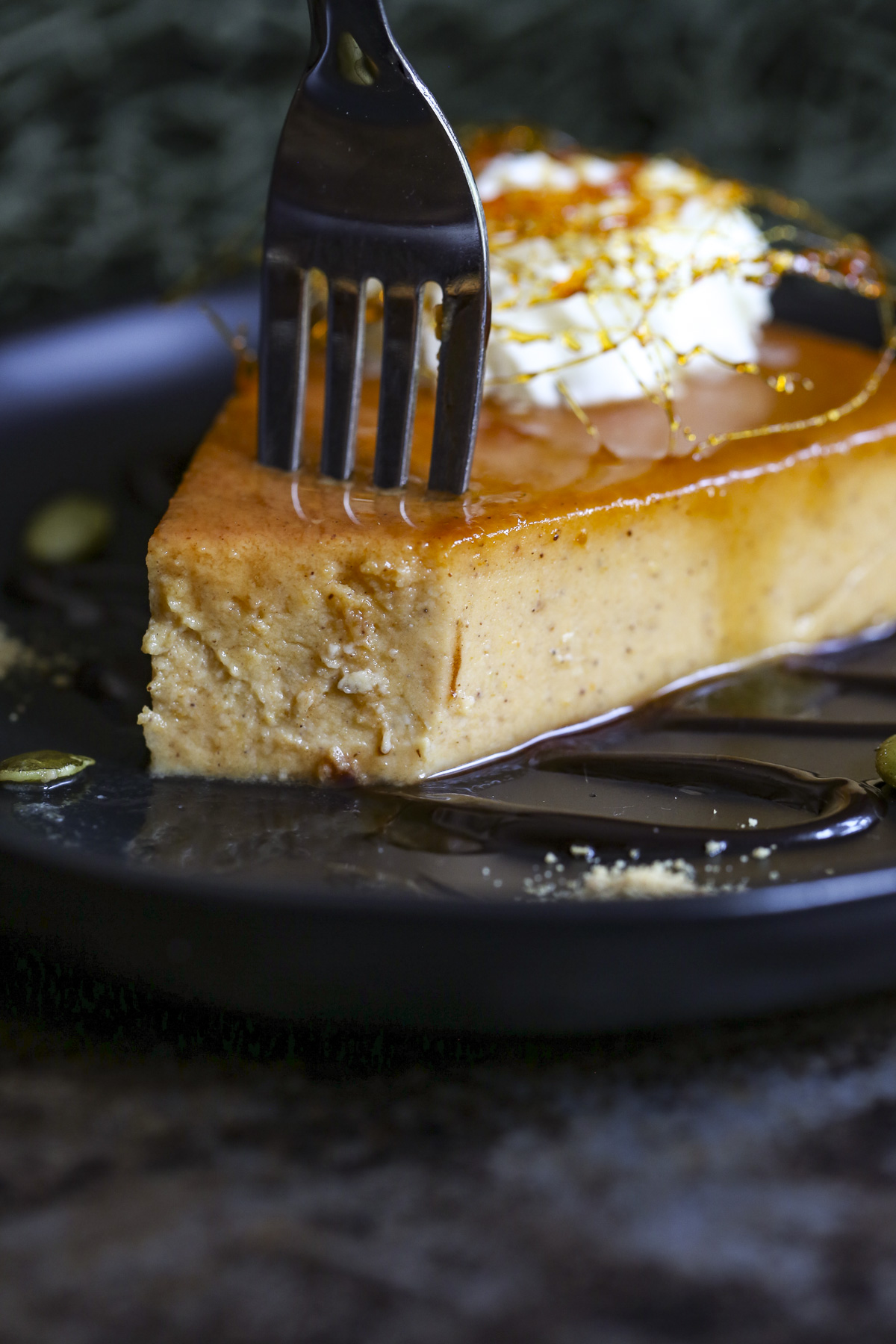 A fork is going into pumpkin flan over a black plate with chocolate drizzle