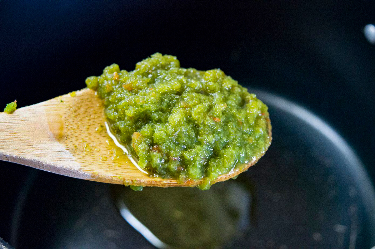 A wooden spoon has sofrito on it over a hot pan with oil.